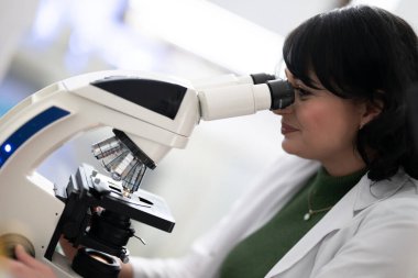Parlak, modern bir laboratuvarda mikroskopla numuneleri inceleyen doktor bilim adamına yakın durun..