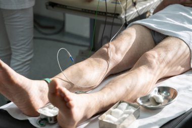 Parlak bir klinikte hasta bacağı üzerinde teşhis ekipmanı kullanan tıp uzmanları. Doktorlar hastalara ekipman tanısı koyuyor.