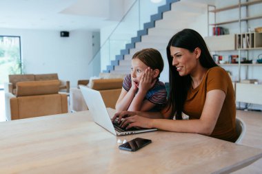Anne ve kızı dizüstü bilgisayarda ailesi ve arkadaşlarıyla konuşuyorlardı. Büyük evin modern oturma odasında oturuyorlardı.