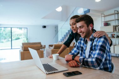 Genç evli bir çift, modern evlerinin oturma odasında otururken bir dizüstü bilgisayarla ebeveynleri, aileleri ve arkadaşlarıyla konuşuyor.