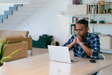 Modern bir oturma odasındaki masada oturan gözlüklü Afrikalı Amerikalı etkileyiciler iş görüşmesi, arkadaşlarla sohbet ve eğlence için dizüstü bilgisayar kullanıyorlar.