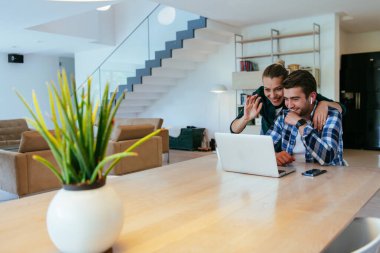 Genç evli bir çift, modern evlerinin oturma odasında otururken bir dizüstü bilgisayarla ebeveynleri, aileleri ve arkadaşlarıyla konuşuyor.