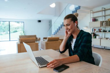 Oturma odasında dizüstü bilgisayar kullanan bir kadın iş arkadaşları ve akrabalarıyla kamera karşısında konuşuyor. Fotoğraf, Job röportajı. Soruları cevaplıyor..