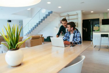 Genç evli bir çift, modern evlerinin oturma odasında otururken bir dizüstü bilgisayarla ebeveynleri, aileleri ve arkadaşlarıyla konuşuyor.