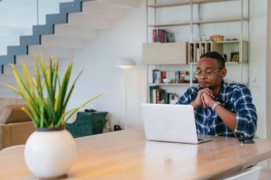 Modern bir oturma odasındaki masada oturan gözlüklü Afrikalı Amerikalı etkileyiciler iş görüşmesi, arkadaşlarla sohbet ve eğlence için dizüstü bilgisayar kullanıyorlar.