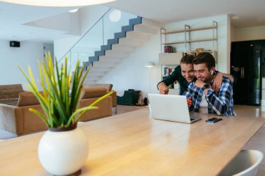 Genç evli bir çift, modern evlerinin oturma odasında otururken bir dizüstü bilgisayarla ebeveynleri, aileleri ve arkadaşlarıyla konuşuyor.