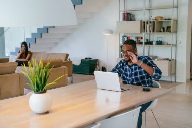 Modern bir oturma odasındaki masada oturan gözlüklü Afrikalı Amerikalı etkileyiciler iş görüşmesi, arkadaşlarla sohbet ve eğlence için dizüstü bilgisayar kullanıyorlar.