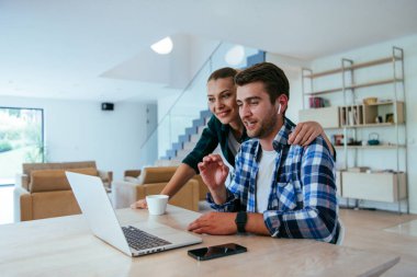 Genç evli bir çift, modern evlerinin oturma odasında otururken bir dizüstü bilgisayarla ebeveynleri, aileleri ve arkadaşlarıyla konuşuyor.