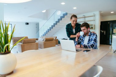 Genç evli bir çift, modern evlerinin oturma odasında otururken bir dizüstü bilgisayarla ebeveynleri, aileleri ve arkadaşlarıyla konuşuyor.