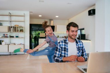 Evden çalışıyorum. Kızı, modern oturma odasında otururken bilgisayarında iş görüşmesi yaparken babasının sözünü kesiyor.