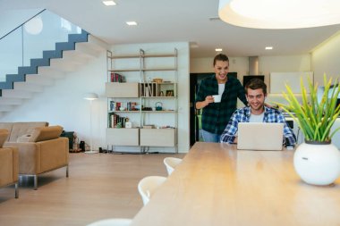 Genç evli bir çift, modern evlerinin oturma odasında otururken bir dizüstü bilgisayarla ebeveynleri, aileleri ve arkadaşlarıyla konuşuyor.