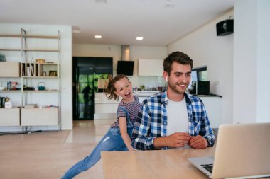 Evden çalışıyorum. Kızı, modern oturma odasında otururken bilgisayarında iş görüşmesi yaparken babasının sözünü kesiyor.