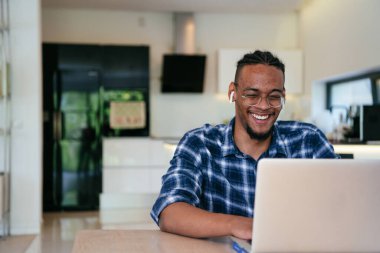 Modern bir oturma odasındaki masada oturan gözlüklü Afrikalı Amerikalı etkileyiciler iş görüşmesi, arkadaşlarla sohbet ve eğlence için dizüstü bilgisayar kullanıyorlar.