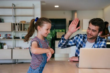 Evden çalışıyorum. Kızı, modern oturma odasında otururken bilgisayarında iş görüşmesi yaparken babasının sözünü kesiyor.