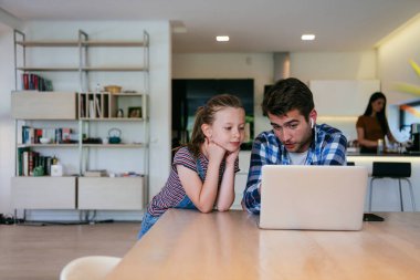 Evden çalışıyorum. Kızı, modern oturma odasında otururken bilgisayarında iş görüşmesi yaparken babasının sözünü kesiyor.