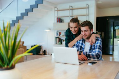 Genç evli bir çift, modern evlerinin oturma odasında otururken bir dizüstü bilgisayarla ebeveynleri, aileleri ve arkadaşlarıyla konuşuyor.