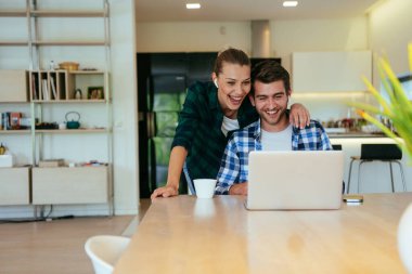 Genç evli bir çift, modern evlerinin oturma odasında otururken bir dizüstü bilgisayarla ebeveynleri, aileleri ve arkadaşlarıyla konuşuyor.