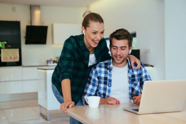 Genç evli bir çift, modern evlerinin oturma odasında otururken bir dizüstü bilgisayarla ebeveynleri, aileleri ve arkadaşlarıyla konuşuyor.