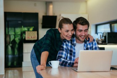 Genç evli bir çift, modern evlerinin oturma odasında otururken bir dizüstü bilgisayarla ebeveynleri, aileleri ve arkadaşlarıyla konuşuyor.