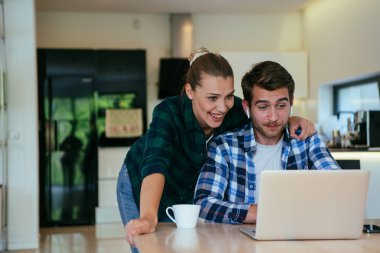 Genç evli bir çift, modern evlerinin oturma odasında otururken bir dizüstü bilgisayarla ebeveynleri, aileleri ve arkadaşlarıyla konuşuyor.