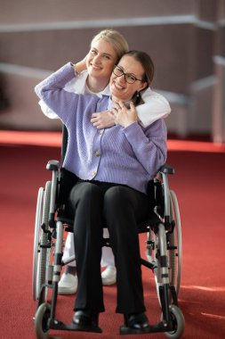 Gülümseyen bir hemşire, tekerlekli sandalyedeki yaşlı bir hastayı kucaklar ve sağlık hizmetlerinde şefkat ve bakım gösterir..