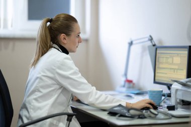 Klinik ortamında bilgisayar üzerinde çalışan beyaz önlüklü kadın doktor. Klinikte bilgisayar üzerinde çalışan kadın doktor.