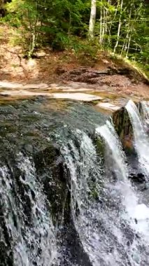 Yeşil ormandaki kayaların üzerinden akan güzel bir şelalenin havadan çekilmiş videosu, temiz su akıntısı olan doğa manzarası, rahatlama ve macera için seyahat yeri. Sinematik ağır çekim dikey