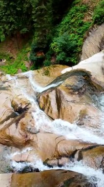 Yeşil ormandaki kayaların üzerinden akan güzel bir şelalenin havadan çekilmiş videosu, temiz su akıntısı olan doğa manzarası, rahatlama ve macera için seyahat yeri. Sinematik ağır çekim dikey