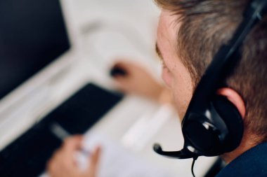 Detaylı bir yakın çekim, çağrı merkezi ortamında yardım sağlarken odaklanmış bir müşteri destek temsilcisini kulaklık takarken yakalar. 