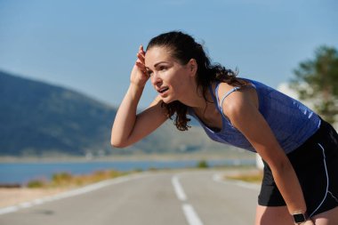 Bir kadın sporcunun dinlenirken, yoğun bir koşunun ardından terleyerek, azim ve kondisyonuna olan bağlılığını somutlaştıran, kendini adamış bir kadın sporcunun nadide görüntüsünü yakına çekiyoruz.