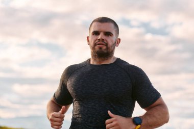 Atletik bir adam güneşin altında koşar, vücudunu yaşam şartlarına şartlandırır. Önündeki yolculuk için azim ve güç yayar.