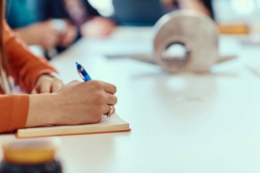 Bir kadın eli, önemli toplantı detaylarını yakalamak için hazırlanma ve odaklanmayı vurgulayan bir kalem tutar..