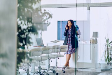 Profesyonel bir iş kadını, çağdaş bir ofis ortamında bulunduğu süre içinde akıllı telefonuyla bir telefon görüşmesi yapar.. 