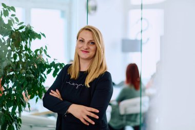 Dengeli esmer bir iş kadını, kollarını şık ve modern ofis binasının önünde kavuşturarak güvenle ayakta duruyor.. 