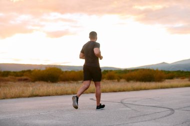 Atletik bir adam güneşin altında koşar, vücudunu yaşam şartlarına şartlandırır. Önündeki yolculuk için azim ve güç yayar.