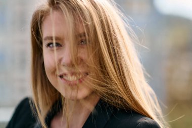 Çarpıcı bir portre siyah takım elbiseli, özgüvenli ve zarif bir iş kadını yakalıyor, terasta zarif bir şekilde poz veriyor hareketli şehir manzarasının arka planına karşı.