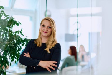 Dengeli esmer bir iş kadını, kollarını şık ve modern ofis binasının önünde kavuşturarak güvenle ayakta duruyor.. 