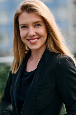 Çarpıcı bir portre siyah takım elbiseli, özgüvenli ve zarif bir iş kadını yakalıyor, terasta zarif bir şekilde poz veriyor hareketli şehir manzarasının arka planına karşı.