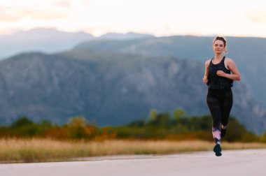 Kararlı bir sporcu güneşin altında kendinden emin bir şekilde koşar. Çevresi göz kamaştırıcı doğal manzaralarla çevrilidir. Zindelik arayışında güç ve direnç gösterir. 