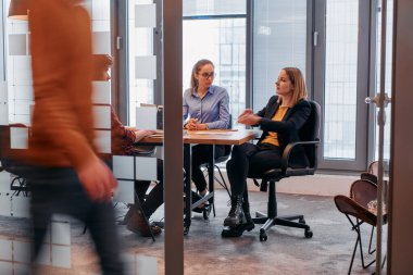 İş ortamının hareketli koşuşturmasında, bir grup genç iş adamı ofislerinin yanındaki koridorda yürürken, meslektaşları içeride iş birliği yaparak,