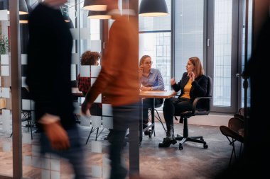 İş ortamının hareketli koşuşturmasında, bir grup genç iş adamı ofislerinin yanındaki koridorda yürürken, meslektaşları içeride iş birliği yaparak,