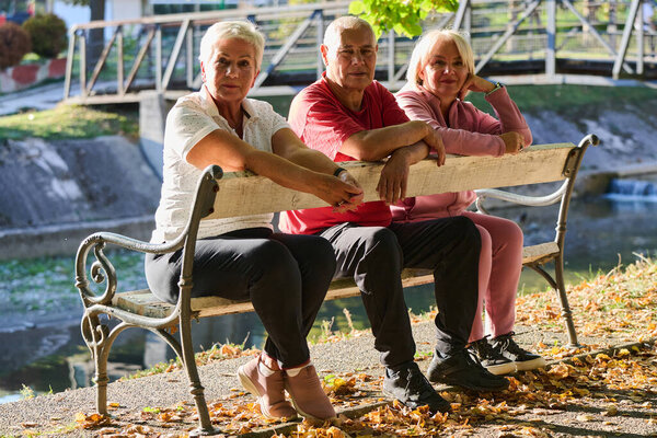 A group of elderly individuals, including a senior man and two older women, sits in a park on a sunny autumn day, embodying the concept of healthy aging through companionship, relaxation, and outdoor