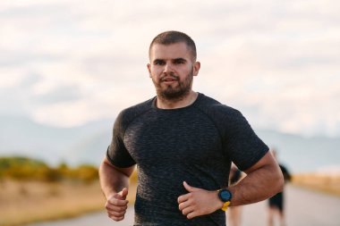 Atletik bir adam güneşin altında koşar, vücudunu yaşam şartlarına şartlandırır. Önündeki yolculuk için azim ve güç yayar.