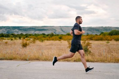 Atletik bir adam güneşin altında koşar, vücudunu yaşam şartlarına şartlandırır. Önündeki yolculuk için azim ve güç yayar.