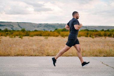 Atletik bir adam güneşin altında koşar, vücudunu yaşam şartlarına şartlandırır. Önündeki yolculuk için azim ve güç yayar.
