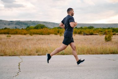 Atletik bir adam güneşin altında koşar, vücudunu yaşam şartlarına şartlandırır. Önündeki yolculuk için azim ve güç yayar.