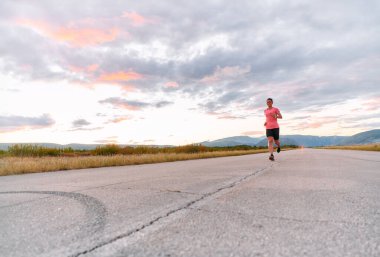 Kararlı bir sporcu güneşin altında kendinden emin bir şekilde koşar. Çevresi göz kamaştırıcı doğal manzaralarla çevrilidir. Zindelik arayışında güç ve direnç gösterir. 