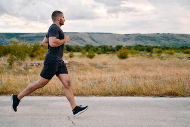 Atletik bir adam güneşin altında koşar, vücudunu yaşam şartlarına şartlandırır. Önündeki yolculuk için azim ve güç yayar.