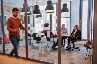 İş ortamının hareketli koşuşturmasında, bir grup genç iş adamı ofislerinin yanındaki koridorda yürürken, meslektaşları içeride iş birliği yaparak,