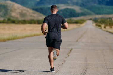 Atletik bir adam güneşin altında koşar, vücudunu yaşam şartlarına şartlandırır. Önündeki yolculuk için azim ve güç yayar.